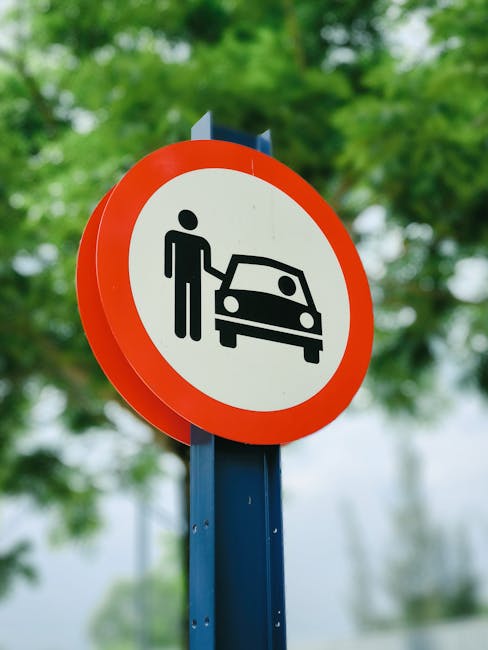 Close-up of a circular traffic sign with a red border, displaying a black pictogram of a person standing next to a car, indicating parking restrictions for vehicles. The sign is mounted on a blue metal pole, with blurred green foliage and a cloudy sky in the background. This type of sign is relevant to house removals and relocation services, as it relates to parking regulations during the loading and unloading process. The scene suggests an outdoor urban or suburban setting, where parking rules may impact home relocation activities. Man with Van Highbury, offering professional removals, is mindful of such regulations when planning furniture transport and packing workflows within Islington.