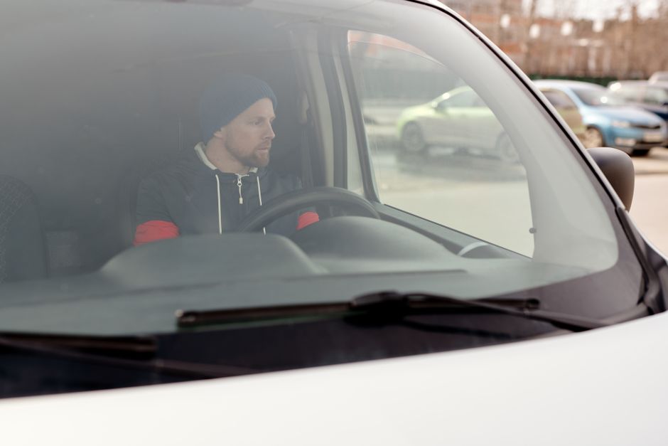 Inside a white moving van with the side door open, two movers from Man with Van Highbury are seated and smiling. The man in the foreground has a dark beard, curly hair, and is wearing a navy blue t-shirt with a logo, while the woman behind him has long dark hair, a black headband, and is dressed in a dark jacket. The van's interior reveals packed cardboard boxes, furniture blankets, and plastic wrap, indicative of a home relocation process. The vehicle is parked on a street with buildings and leafless trees visible in the background, suggesting an urban setting. The scene captures the loading or unloading phase of furniture transport and packing for a move, aligned with regulations for parking during removals in Islington as detailed on the webpage. Man with Van Highbury provides local and long-distance moving services, supported by careful handling of household items, equipment like trolleys and straps, and efficient loading procedures.